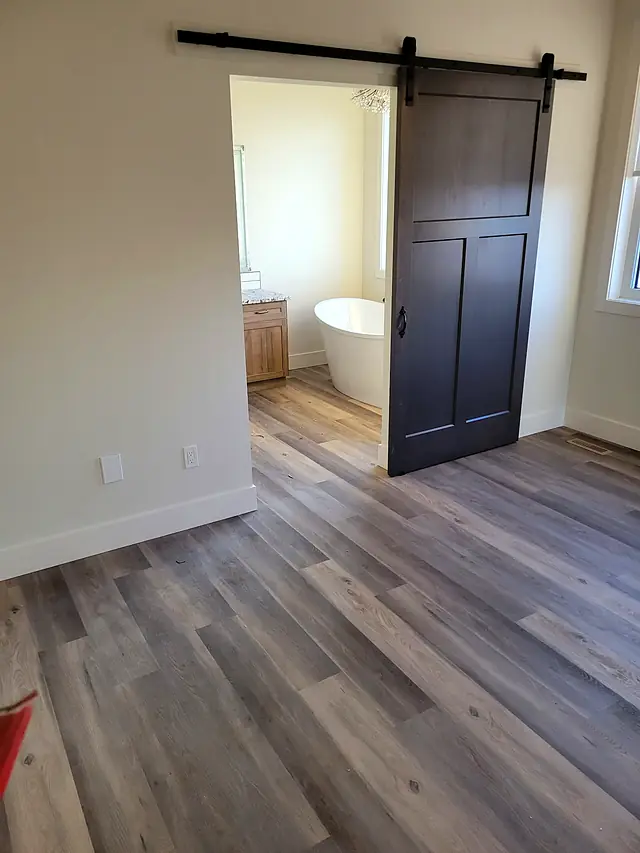 Bedroom with a barn door and gray-brown plank flooring