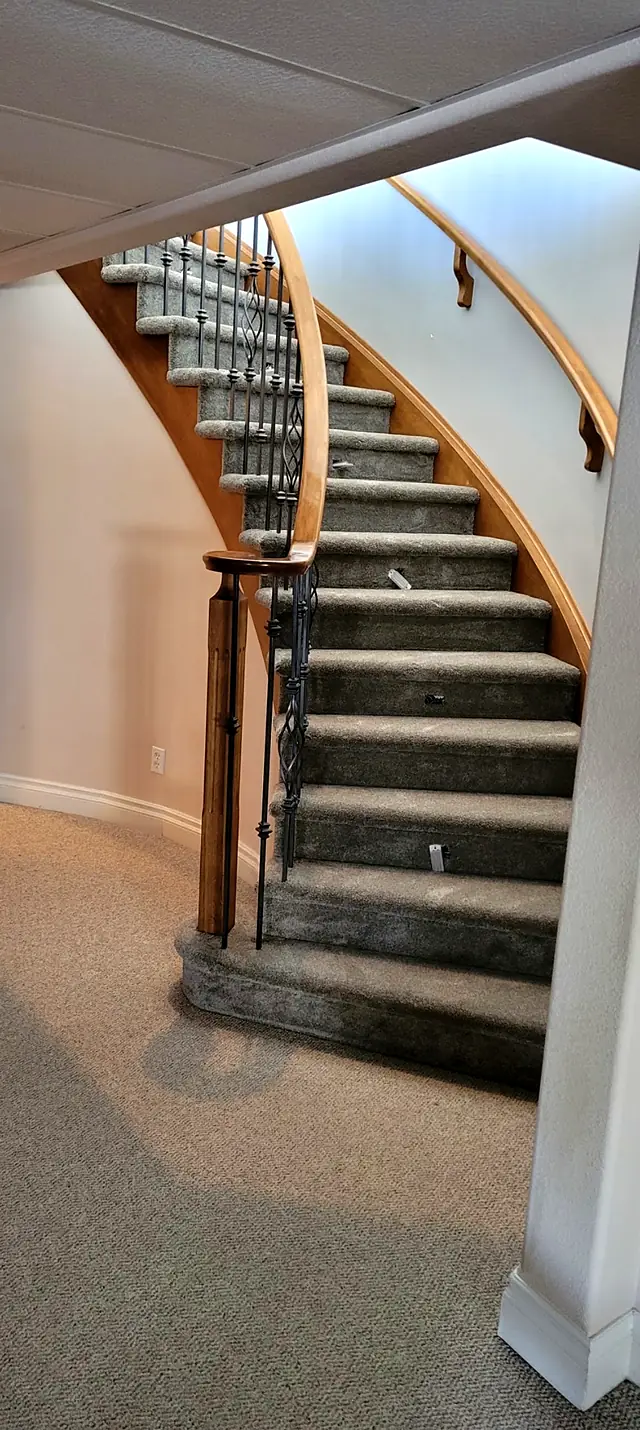 Curved staircase with gray carpeted treads and a wood handrail